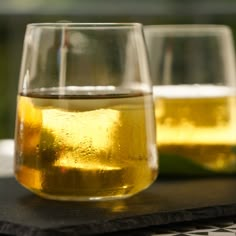 two glasses filled with yellow liquid sitting on top of a table next to each other