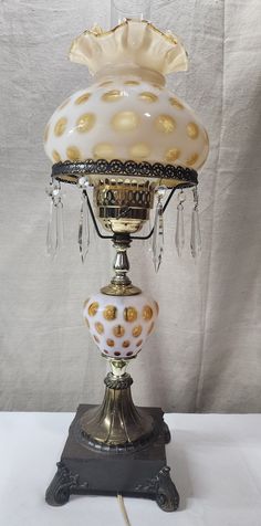 an old fashioned lamp is sitting on top of a white cloth covered tablecloth with gold dots and crystal drops hanging from it's sides