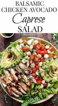 a salad with chicken, avocado and tomatoes in it on top of a wooden table