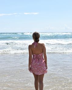 a woman standing on the beach looking out at the ocean with her back to the camera