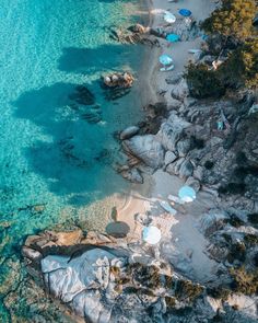 an aerial view of the beach with umbrellas and rocks in clear blue ocean water