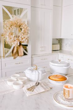 a white kitchen counter topped with lots of dishes and bowls filled with cake next to a candle