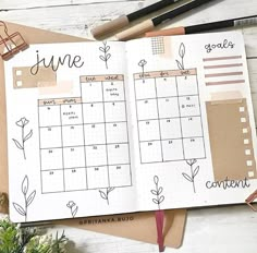 an open planner book sitting on top of a table next to flowers and pencils