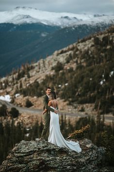 a bride and groom standing on top of a mountain