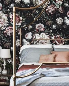 a bed sitting next to a wall with flowers on it and a clock above the headboard