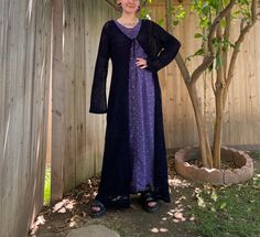 a woman standing in front of a tree wearing a purple dress and black cardigan