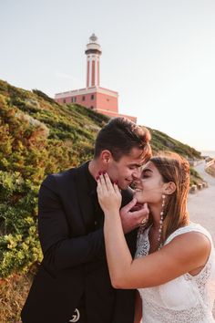 a bride and groom standing next to each other in front of a lighthouse