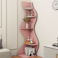 a pink curved shelf with books and vases on it next to a wall clock