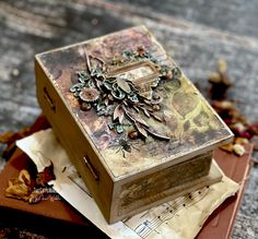 an altered box sitting on top of a piece of paper next to some dried leaves