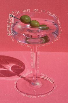 two olives in a martini glass on a pink surface