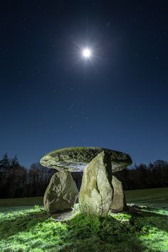 the moon shines brightly in the night sky over a stone bench and moss covered ground