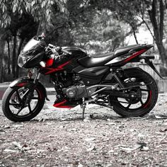 a black and red motorcycle parked in front of some trees with leaves on the ground