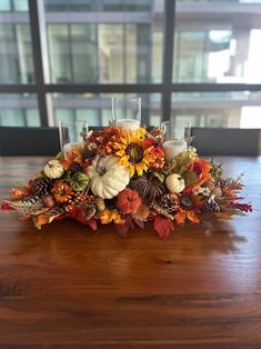 a centerpiece with candles and flowers on a wooden table in front of a window