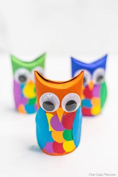 three brightly colored owls sitting next to each other on a white surface with one looking at the camera