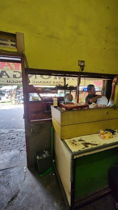 a man sitting at a counter in front of a yellow and green booth on the street