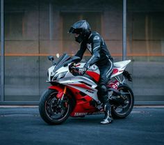 a person on a red and white motorcycle in front of a building with glass windows