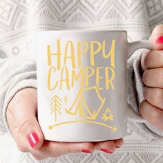 a woman holding a coffee mug with the words happy camper on it in gold