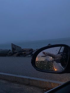 the side view mirror of a car with rocks in the back ground and water behind it