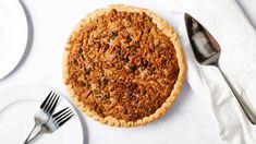 a pie sitting on top of a white table next to silverware and forkes