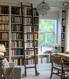 a living room filled with lots of books next to a table and chair in front of a window