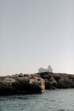 a lighthouse on top of a rocky outcropping next to the ocean with a small house in the distance