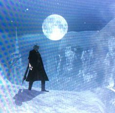 a man standing on top of a snow covered slope next to a giant white moon