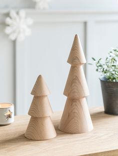 three wooden christmas trees on a table next to a candle holder and potted plant