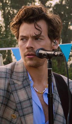 a man with curly hair standing in front of a microphone and wearing a plaid jacket