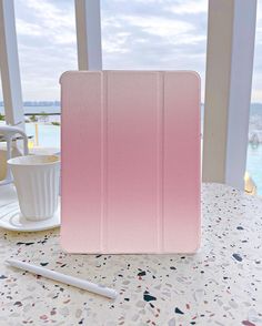 a pink ipad case sitting on top of a table next to a cup and pen