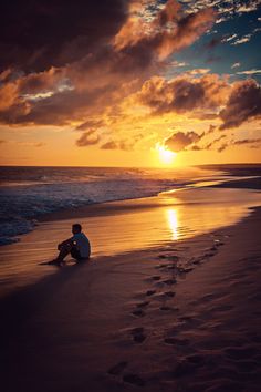 a man sitting on top of a beach next to the ocean under a cloudy sky