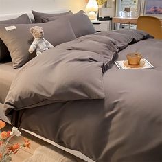 a teddy bear sitting on top of a bed in a room with gray sheets and pillows