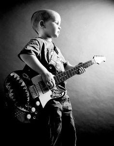 a young boy is holding a guitar and posing for a black and white photo in the studio