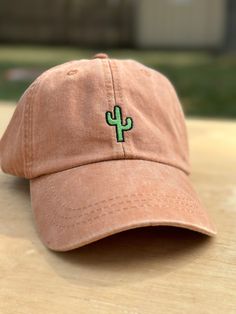 a pink hat with a green cactus embroidered on the front sits on a wooden table