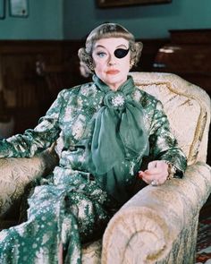 a woman sitting on top of a couch wearing a green dress and black eye patch