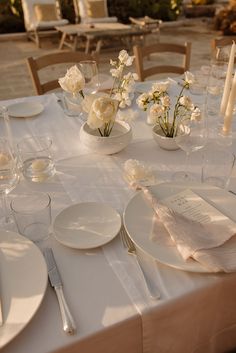 the table is set with white flowers and place settings for two people to sit at