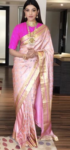 a woman in a pink and gold sari standing on a rug with her hand on her hip