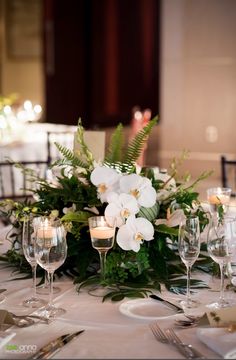 the table is set with white flowers and greenery for an elegant centerpieces