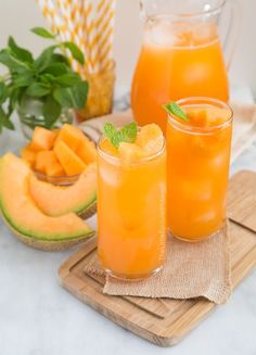 two glasses filled with orange juice and garnished with mint on a wooden tray