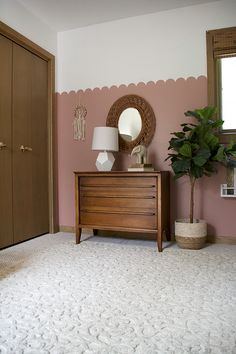 a room with a dresser, mirror and potted plant on the floor in front of it