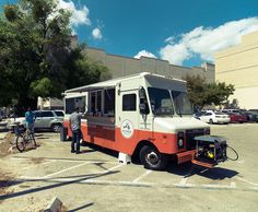 an orange and white food truck parked in a parking lot with two men standing next to it