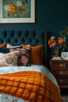 a bed with orange and blue pillows on top of it next to a dresser filled with flowers