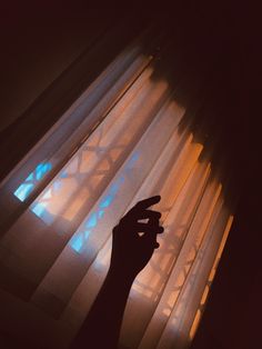 a person's hand is pointing at the light coming through the blinds in front of them