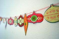 christmas ornaments are hanging on a line with red and green paper decorations in the shape of an ornament