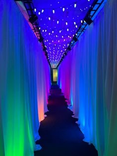 a long hallway with blue and green lights on the ceiling, along with drapes draped in white fabric