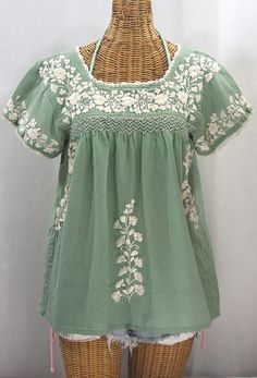 a woman's green top with white flowers on the front and back, sitting on a wicker mannequin