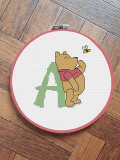 a cross stitch pattern with the letter a and a teddy bear in a red shirt