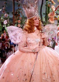 a woman in a pink dress and crown holding an umbrella