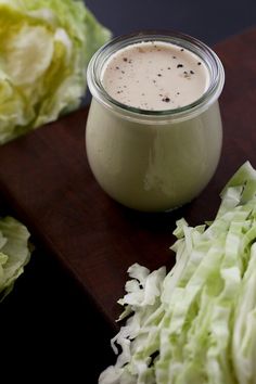 lettuce and dressing in a small glass jar on a wooden cutting board next to some lettuce leaves