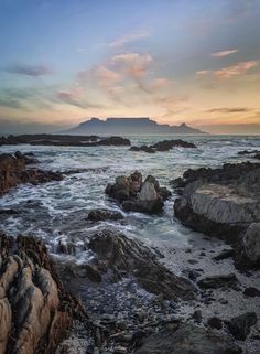 the sun is setting over the ocean and rocks