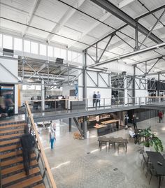 people are walking through an open building with tables and chairs in the middle of it